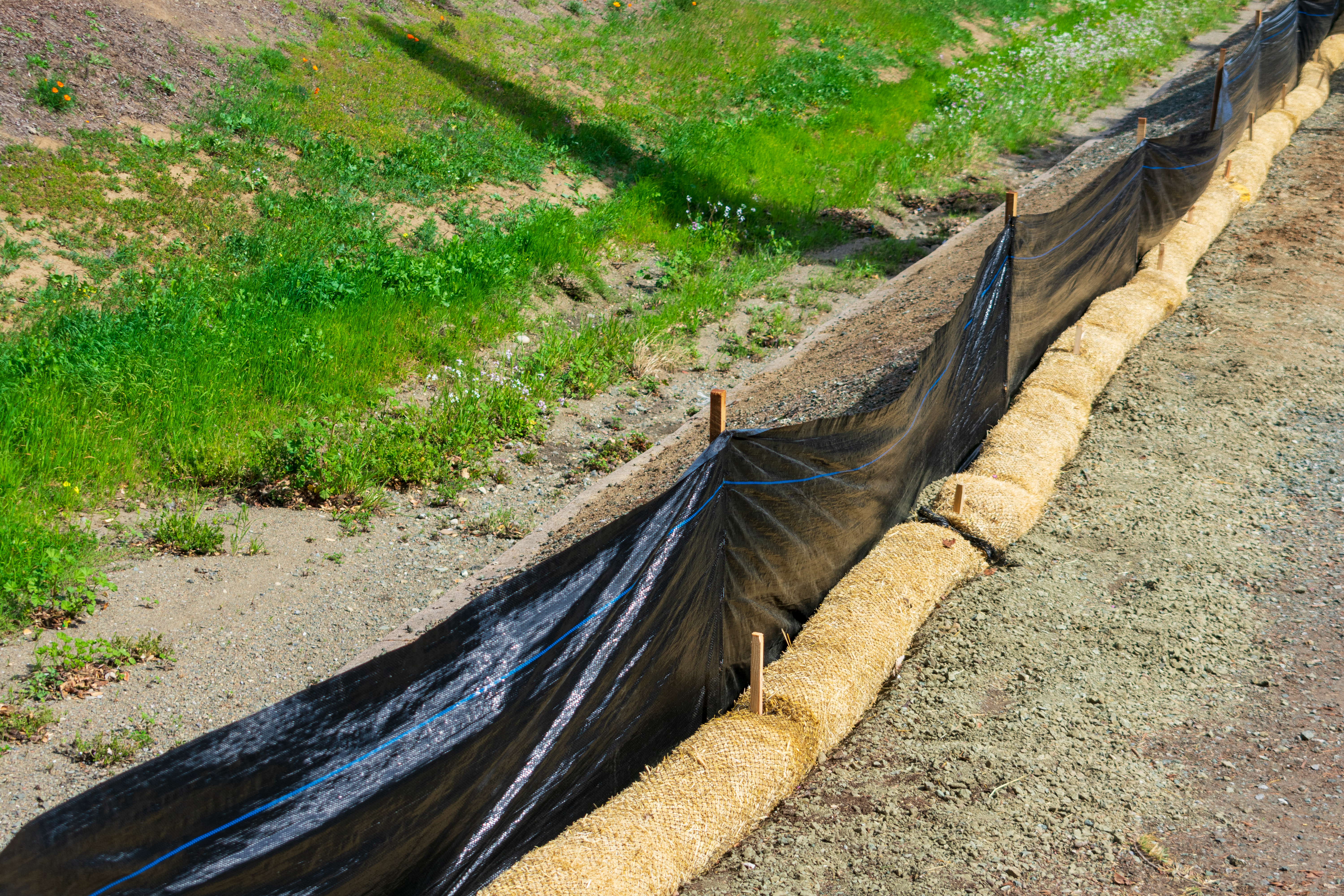 Straw wattles and plastic fence placed along dry waterway to reduce soil erosion, debris runoff and retain sediment during construction and maintenance project.